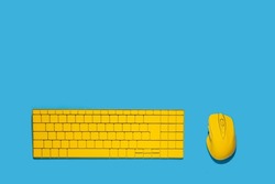 Yellow keyboard and yellow computer mouse on a blue background. Top view, flat lay.