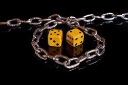 Gambling addiction. Two dice wrapped in a chain on a black background with reflection. Selective focus