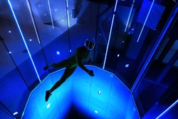 A man flier doing stunts in an indoor wind tunnel with neon lights