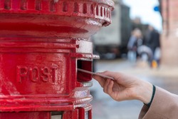 Throwing a letter in a red British post box from the side