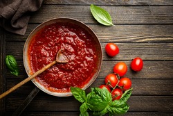 Classic homemade Italian tomato sauce with basil for pasta and pizza in the pan on wooden background, top view.
