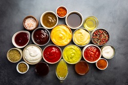 Set of different bowls of various dip sauces, on dark background, top view