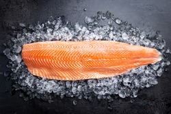 Fresh raw salmon or trout sea fish fillet on ice on black background, top view