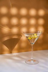 Cocktail vodka martini with green olives on orange background with bright beautiful shadows