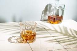 Whiskey with ice in glasses and bottle, white background with hard light, shadows and sun glare, copy space