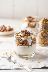 Crunchy granola with yogurt, banana, nuts, chocolate and honey in a glass on white background. Healthy breakfast concept.