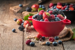 Ripe sweet different berries in red bowl on rustic wooden table. Harvest Concept