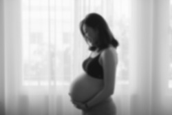 Portrait of young pregnant attractive woman, standing by the window ,out of focus in blackandwhite tone