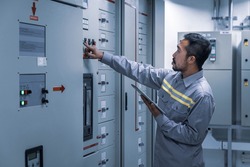 Electrical engineer working check the electric current voltage and overload at front of load center cabinet or consumer unit for maintenance with tablet in main power distribution system room.
