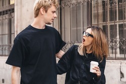 Couple walking outdoor, they hug. Woman look shocked with open mouth on her man and hold coffee take away. Unfaithful relationship concept. Wife suspects her husband is disloyal. Furious woman.