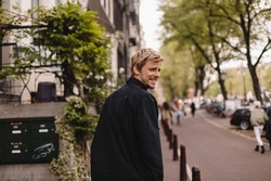Portrait of blonde man wear black shirt walk in city street. Young man turned back and looked at the camera. Lifestyle. Man look happy and smiling.