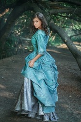 A young woman in a 19th century dress runs away along a forest path, a mystical atmosphere. Historical costume. Woman in a park or forest.