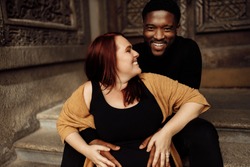 Close up charming African American man hug pregnant belly of beautiful white woman, happy couple expect for a baby, excited about parenting, motherhood and fatherhood concept