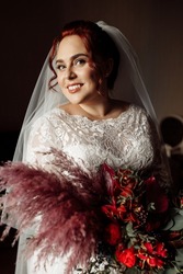 Portrait of gorgeous adorable bride holding big wedding bouquet. Beautiful pretty woman look at the camera, smiling, excited about marriage. Attractive adult lady wearing stylish bridal white dress.
