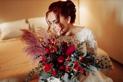 Portrait of gorgeous adorable bride holding big wedding bouquet. Beautiful pretty woman look at the camera, smiling, excited about marriage. Attractive adult lady wearing stylish bridal white dress.