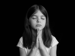 young girl prays, portrait on a dark background, black and white photo