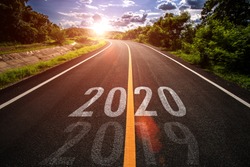 The word 2020 written on highway road in the middle of empty asphalt road at golden sunset and beautiful blue sky. Concept for new year 2020.