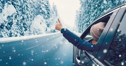 Happy woman in the car gesture finger up on the snowy background.