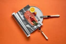 fresh salmon with lemon in foil paper, ready for cooking in oven on orange background