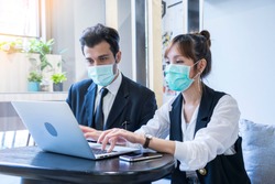 Asian female and Businessman workers meeting together with laptop and wear protective masks prevent PM 2.5 and corona virus or covid19 at co working space .Health and teamwork concept