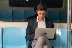 A business man sitting on a laptop working on the subway in the morning on his way to work 