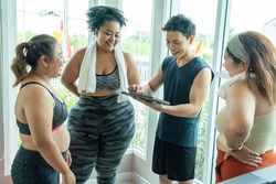 Three fat women, plus size women wearing sporeware outfits talking with trainer hold tablet ask informaion in class. Healthy weight loss in the gym Relationship concept and fat girl exercising

