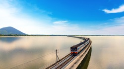 Aerial view of amazing Thailand travel train look like floating above the lake of Pa Sak Jolasid dam with blue sky. Unseen Train is running on the railway bridge over the reservoir at Lopburi Thailand