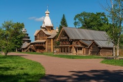 View of the Church of the Assumption of the Virgin and the log house in the Novgorod Museum of Folk Wooden Architecture of Vitoslavlitsa on a sunny summer day, Veliky Novgorod, Russia