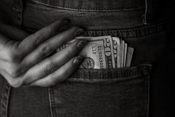 Teenage girl grabs dollar banknotes from her back pocket. Banknotes close up, money in a jeans pocket. Dollars stick out of the jeans pocket, money currency concept