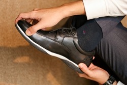 A man in a white shirt and dress pants laces up black shoes in a hotel room. Stylish groom putting on shoes close-up and getting ready for the wedding day. Morning wedding preparation.
