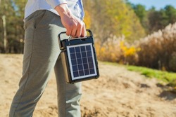 The guy is carrying a portable solar charging station in his hands. Eco-friendly energy for camping and outdoor recreation. Solar panel with battery