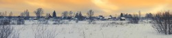 Winter panorama with beautiful sunset over the russian village and the snow-covered field under an orange sky