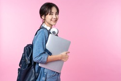 Portrait of smiling young Asian college student with laptop and backpack isolated over pink background