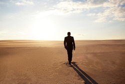 A man in a suit walks through the desert, loneliness, pursuit of his goal, the hot sun, a man lost in the desert, a businessman at the beginning of his journey, forward movement, willpower