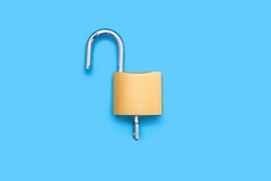 Opened padlock with a key on a blue background, top view. An open gold-colored lock with a key on a uniform blue background. The concept of protection or access in the form of a lock and key