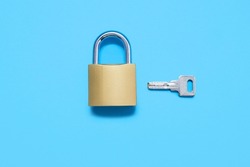 Padlock with a key on a blue background, top view. A gold-colored lock with a silver key on a uniform blue background. The concept of protection and security in the form of a lock and key