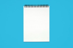 Notebook made of white paper with binding on a blue background. Blank notepad with free space for text. Notebook in classic binding without notes, top view
