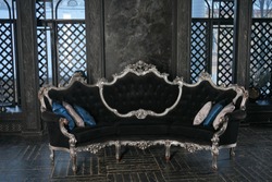 expensive black with silver retro sofa on the background of Windows with daylight in a large dark room with wooden floor