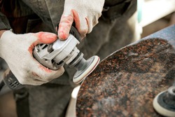 a man in work clothes and gloves polishes a marble stone with an angle grinder. grinding stone. manufacturing of monuments. marble slab. man with a tool