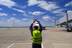 male airport marshal with wands in a yellow uniform helps park the plane