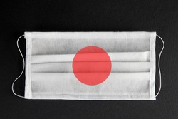 Coronavirus update in Japan. Japanese healthcare concept. Flag of Japan printed on medical mask on black background. Covid-19 outbreak.  Spread of corona virus in Asia.