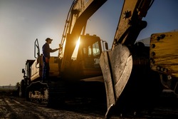 Sunset on the construction site. Silhouette of a contractor builder is sitting near bulldozer. Construction machinery concept