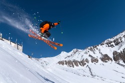 A male athlete skier in an orange trigger makes a jump jump with a grab with flying snow powder against the background of Mount Elbrus in the North Caucasus. Winter Extreme Sports Concept