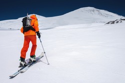 Ascent of a skier with a backpack in a mask and sunglasses on skis with poles to go uphill for freeride and backcountry. North Caucasus. Climbing Volcano Elbrus