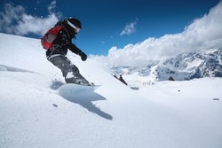 Young woman snowboarder in deep snow - extreme freeride on the background of snow-capped mountains on a sunny day