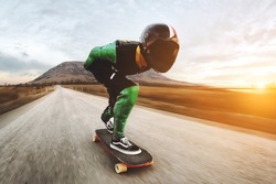 A young man in helmet and a leather suit in a special rack rides a longboard on afsaltu on background mountains and beautiful sky