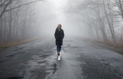 Lonly woman  walk away into the misty foggy road in a dramatic mystic scene. Girl walking in a foggy autumn landscape