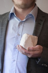 Man in a suit and shirt holding a white stone in front of him.