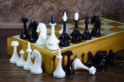 Vintage large plastic chess on the corner of the board in random order on a dark brown background