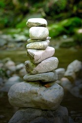 Pile of stacked rocks, in bright sunlight. Rock balancing in a riverbed. Rocks laid flat upon each other to great height. Balanced rocks, surrounded by water at the creek. An art form or hobby. Photo.